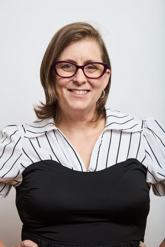 A woman with shoulder-length brown hair wearing glasses and a black and white striped blouse, representing MSB Leadership, smiles at the camera against a plain white background.